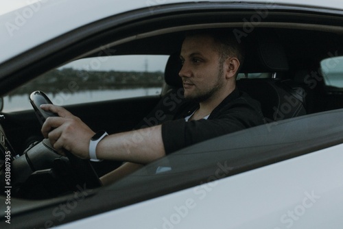 Handsome man driver with black sunglasses in black T-shirt and white shirt sits in modern white sport car and looks at the sunset outdoors. Fresh weekend out of city near riverside. Dark tone photo  © Евгения Жигалкина