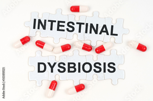On a white surface, tablets and puzzles with the inscription - INTESTINAL DYSBIOSIS photo