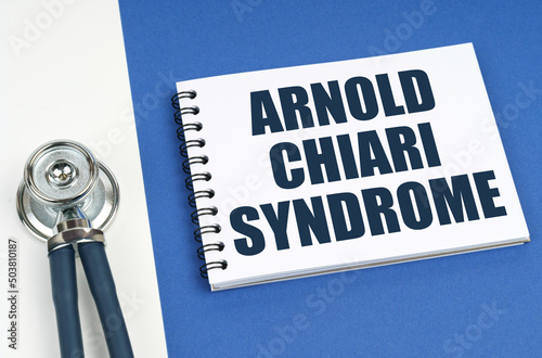 On a blue-white surface lies a stethoscope and a notepad with the inscription - Arnold Chiari Syndrome