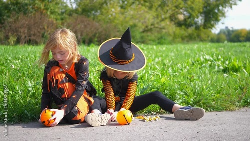 Two girls in hats and witch costumes share the loot. Girls shake out candy from buckets in the shape of pumpkins. Halloween day celebrations. photo
