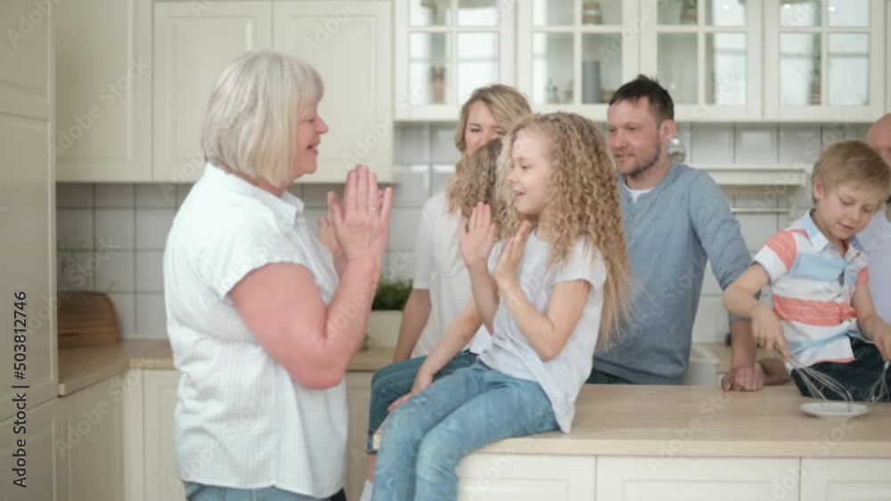 Large European family gathered in kitchen of apartment. Three generations together at home. Happy parents chat and laugh together in kitchen. grandma plays with granddaughter claps hands