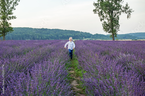 Blond boy of school age. Child runs through purple lavender field in summer.