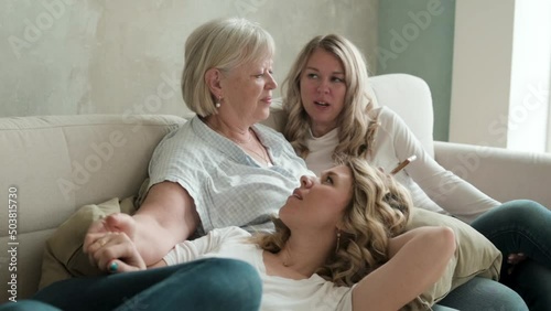 Happy family. older mother with two twin daughters are sitting on cozy sofa. adult daughter put head on mother's lap. Communication of happy parents with adult children. two generations. Mother's Day