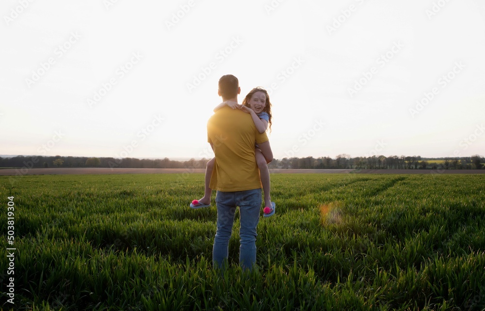 father carrying his daughter whilst walking in a field at sunset father carrying his daughter whilst walking in a field at sunset