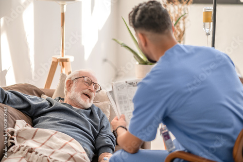 Caring caregiver entertaining male patient during the intravenous therapy photo