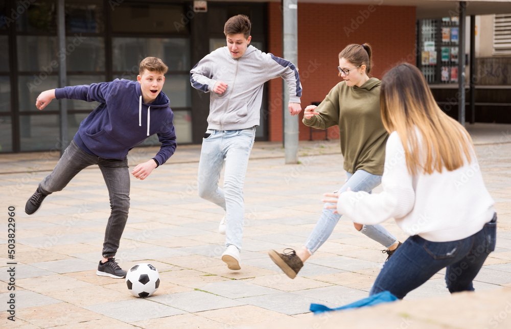 Group of teenagers playing soccer with ball outdoors and having fun