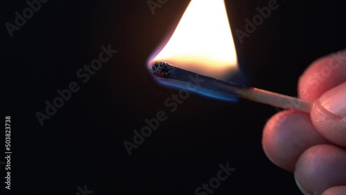Hand with burning matchstick on a dark background. 