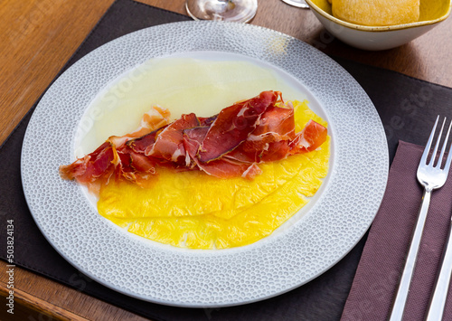 Top view Elegant Appetizer - Melon and pineapple carpaccio with thinly sliced jamon on white plate close up photo