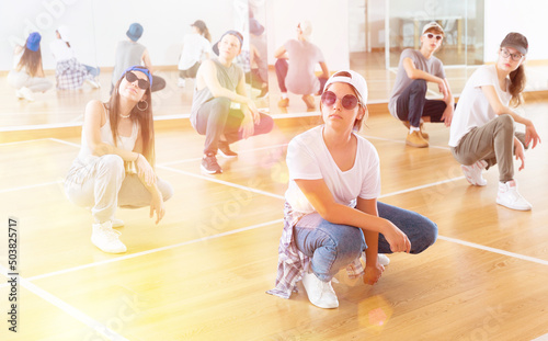 Positive teen girls and boys hip hop dancers squatting during group dance workout