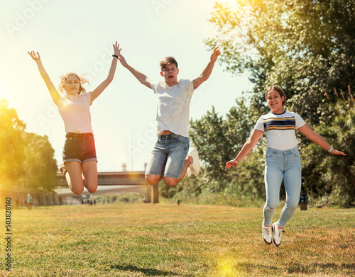 Group of teenagers having fun together outdoors, jumping on green lawn in summertime