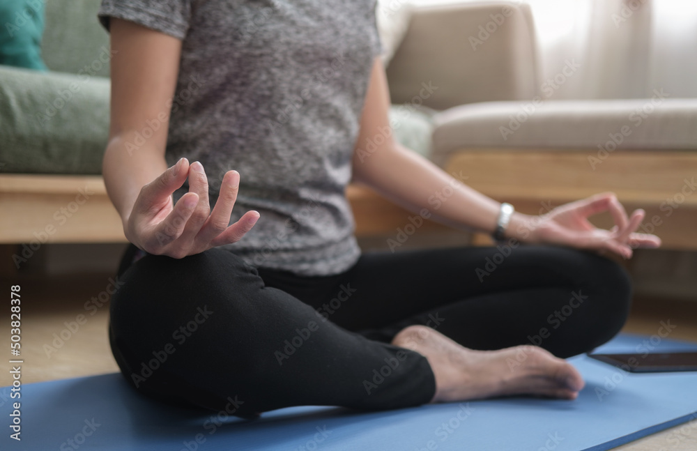 Healthy woman practicing yoga at home, sitting in lotus pose to meditation. Healthy lifestyle, meditation concept.