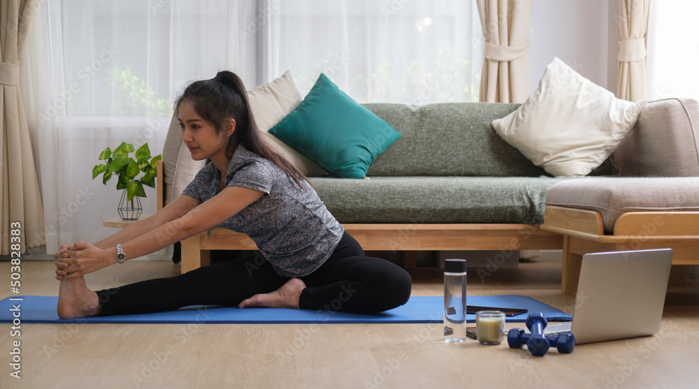 Young woman sitting on mat and stretching legs before workout at home. Fitness and healthy lifestyle. Young woman sitting on mat and stretching legs before workout at home. Fitness and healthy lifestyle.