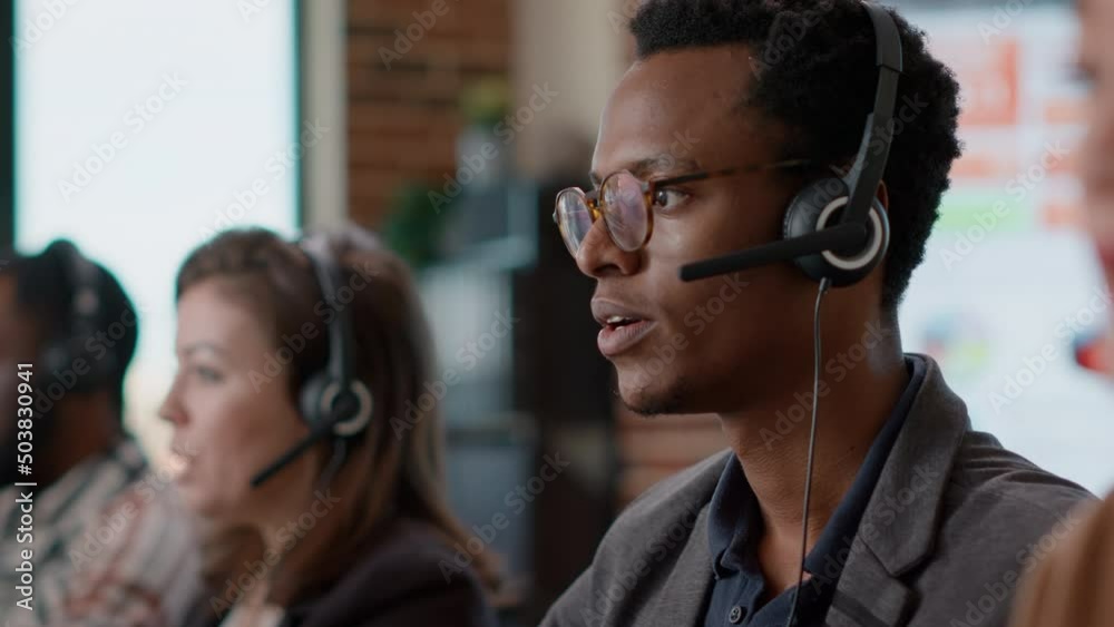African american worker having conversation on headset with client, offering telemarketing assistance at call center. Man with headphones and microphone working at customer service. Close up.