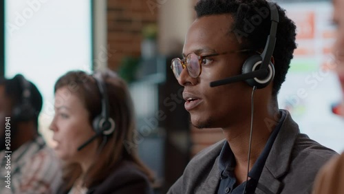 African american worker having conversation on headset with client, offering telemarketing assistance at call center. Man with headphones and microphone working at customer service. Close up. photo