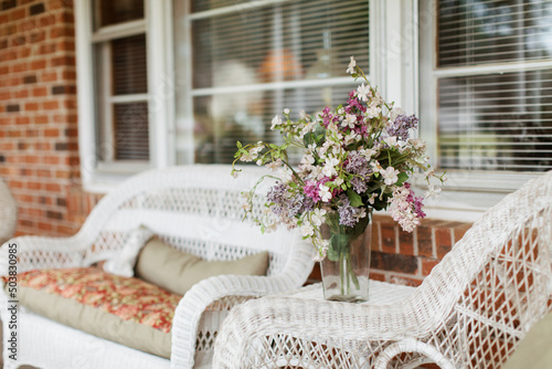 Fotografie A based flower bouquet and white whicker furniture on a red brick front porch