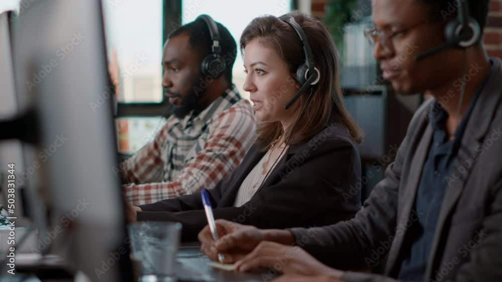 Young woman using audio headset and computer at call center job, offering helpline assistance to people. Female consultant talking to clients at customer care service, helping with telemarketing.