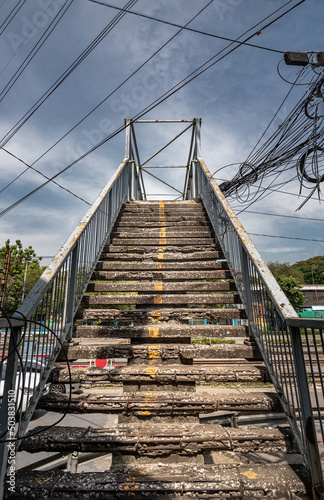 Fototapeta Naklejka Na Ścianę i Meble -  Old cement mortar stairs and steps was left to deteriorate over time. Cement is broken and show internal rebar structure elements, Pedestrian overpass and yellow lines dividing the traffic channel. 