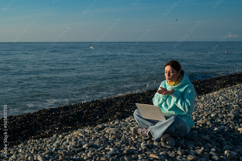 Caucasian woman communicating by video call on laptop on pebble beach. 