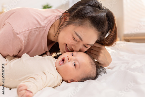 New asian mom playing to adorable newborn baby on bed smiling and happiness at home.Mom talking with infant baby and kissing on baby cheek with love.Baby and Mother day concept