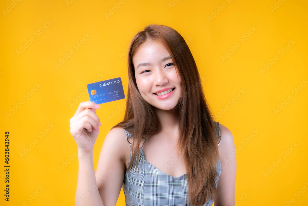 Asian girl showing credit card for payment shopping online and - paying by credit card isolated on yellow - online shopping e-commerce telemarketing concept Asian girl showing credit card for payment shopping online and - paying by credit card isolated on yellow - online shopping e-commerce telemarketing concept
