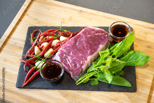 Close up from flatlay, top table view of Raw Beef herb ingredients, basil, garlic, chilli, sauces on black slate plate for Thai cooking menu, Stir-fried beef basil. photo