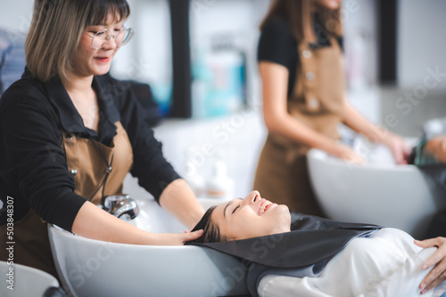 young beautiful woman client getting hair treatment in beauty salon with professional female stylist hairdresser  using shampoo and water on person head to clean and coiffure hair fashion service
