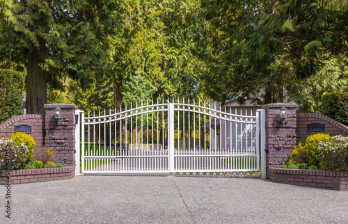 Iron front gate of a luxury home. Wrought iron white gate and brick pillar