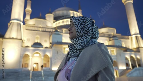 A Muslim woman in a headscarf or hijab pose in front of the Kocatepe mosque in the evening