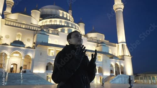An Asian Muslim man pose with hand praying in front of the Kocatepe mosque in the evening