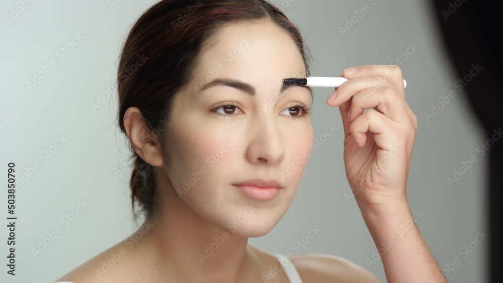 Makeup tutorial: gorgeous hispanic woman in studio uses eyebrow brush Makeup tutorial: gorgeous hispanic woman in studio uses eyebrow brush
