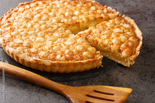 Caramel macadamia tart baked in a buttery homemade shortcrust pastry closeup in the board on the table. Horizontal