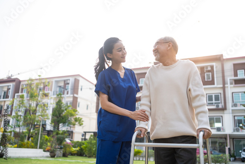 Asian young caregiver nurse support senior older male walking outdoors