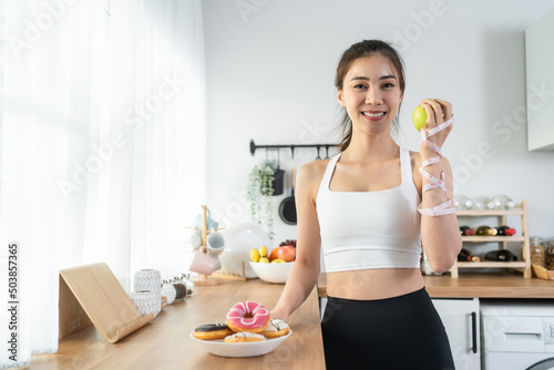 Asian attractive active woman holding green apple in kitchen at home.