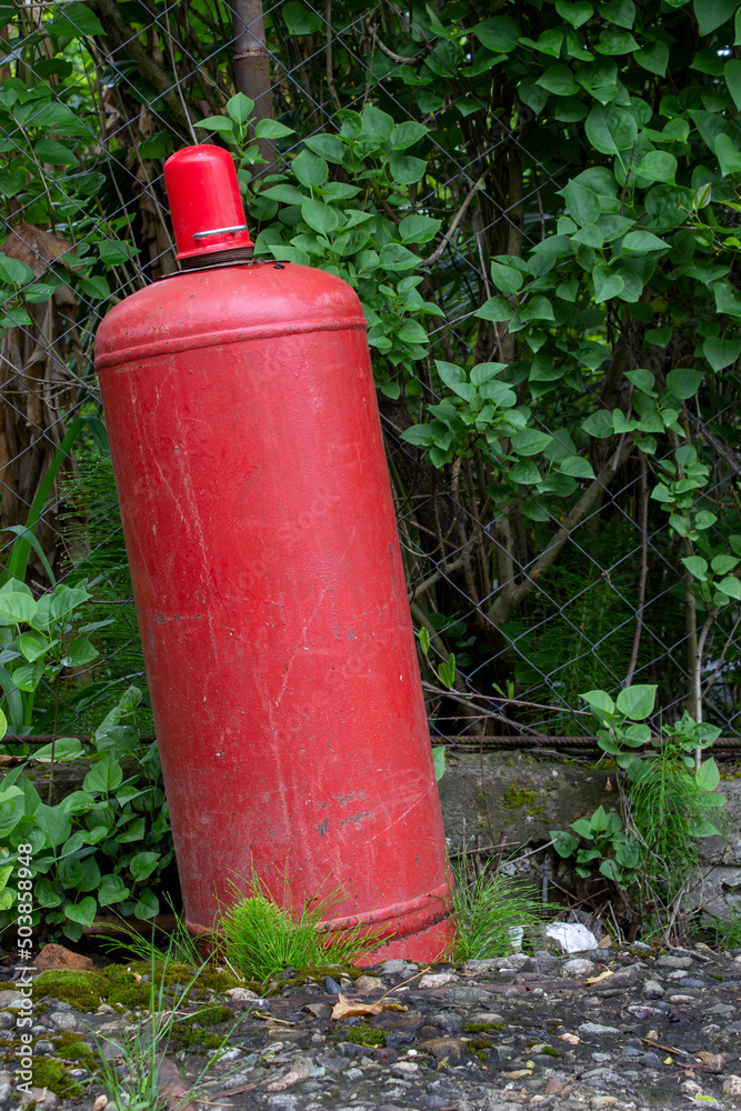 Red gas cylinder in the village. Rising gas prices. Saving gas consumption. Expensive gas. Red gas cylinder in the village. Rising gas prices. Saving gas consumption. Expensive gas.