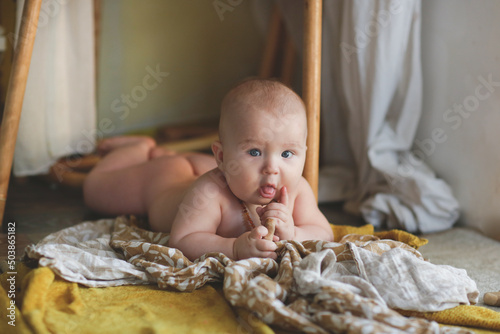 cute european baby 5 months old lies on a blanket on the floor. A child wearing amber teething beads in a real interior