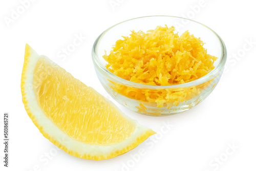 Grated lemon zest in a glass bowl next to lemon segment.