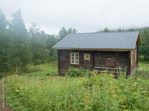 View of STF Njunjes Mountain cabin on a meadow  moody rainy day with thick fog. Wooden cottage lies on the banks of the Tarra river  at Padjelantaleden hiking trail. Lapland summer landscape