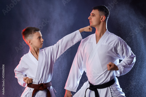 Boy practicing karate with instructor on dark background photo