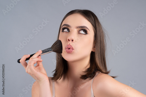 Fényképezés Portrait of a funny beautiful young girl with makeup blusher brush, bright make-up