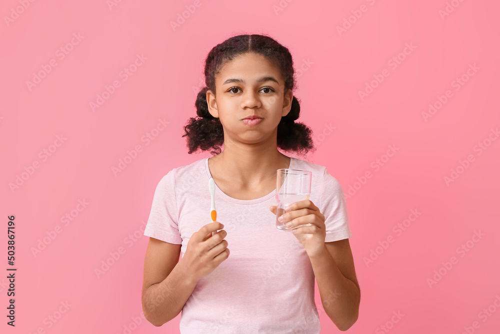 African-American teenage girl with glass of water and toothbrush on pink background African-American teenage girl with glass of water and toothbrush on pink background