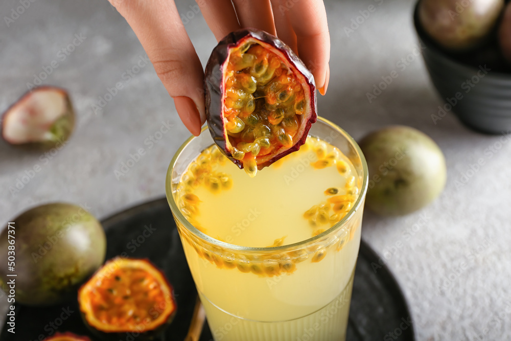 Woman squeezing passion fruit in glass on grey background - obrazy, fototapety, plakaty 