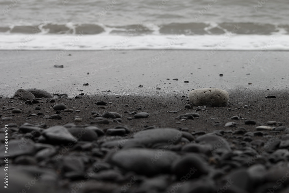 Black volcanic beach with surf wave, black sand, cobbles as lines with blur, texture, background. Black volcanic beach with surf wave, black sand, cobbles as lines with blur, texture, background.