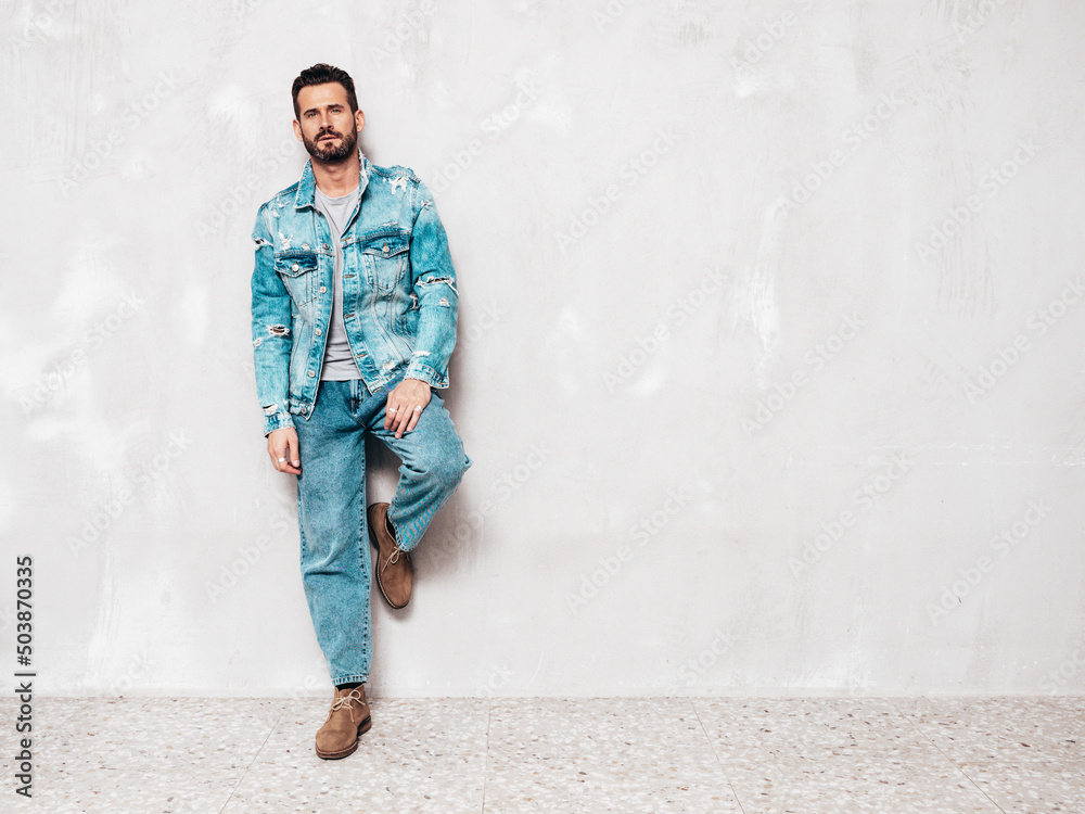 Portrait of handsome confident stylish hipster lambersexual model. Sexy man dressed in jeans jacket. Fashion male isolated on grey wall in studio. Full length Portrait of handsome confident stylish hipster lambersexual model. Sexy man dressed in jeans jacket. Fashion male isolated on grey wall in studio. Full length