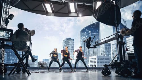 Leinwand Poster Music Clip Studio Set: Shooting Hip Hop Video Dance Scene with Three Professionals Dancers Performing on Stage with Big Led Screen with Modern City Background