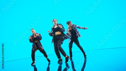 Diverse Group of Three Professional Dancers Performing a Hip Hop Dance Routine in Front of a Big Digital Led Wall Screen with Turquoise and Blue Color Background in Studio Environment.
