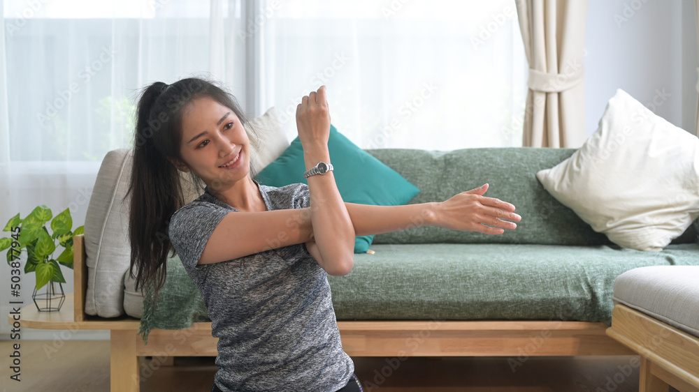 Smiling young woman warming up, stretching arms before workout at home. Smiling young woman warming up, stretching arms before workout at home.