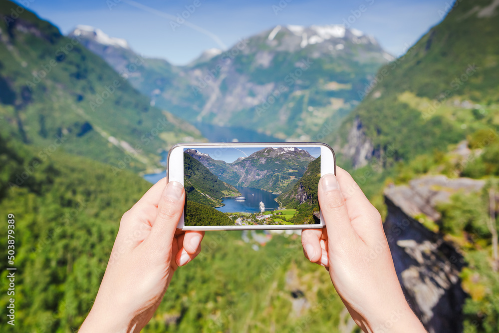 Female hand with phone photographing famous places of Geiranger fjord, Norway