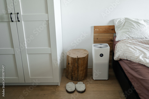 Technologies for health. The air purifier stands on the floor in the bedroom next to the bed and cleans the air of dust. photo