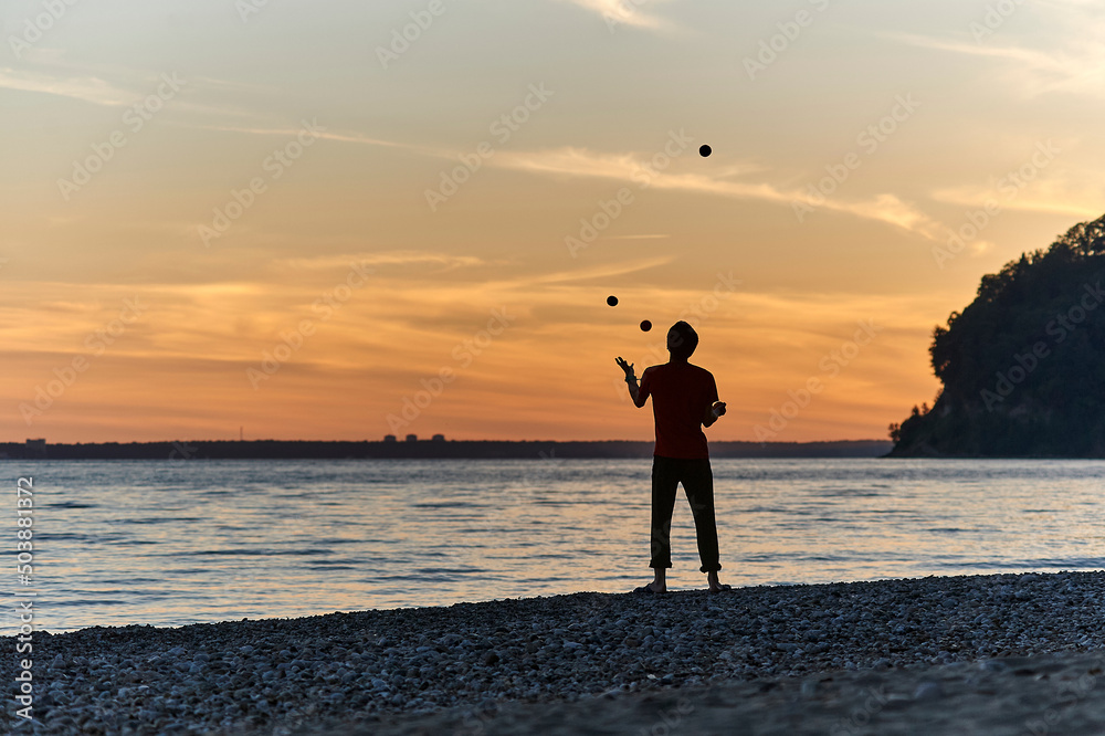 The guy stands on the seashore at sunset and juggles with fruits