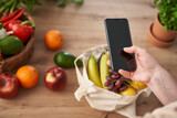 Woman using mobile phone with shopping bag full of fruits and vegetables